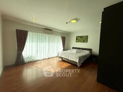 Spacious bedroom with large window and elegant curtains, featuring a cozy bed and wooden flooring.