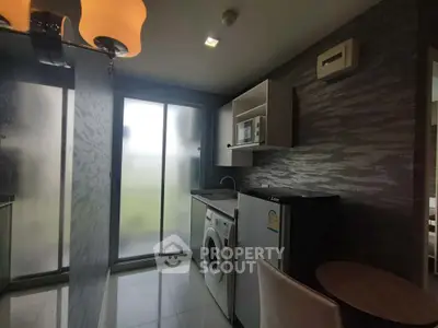 Modern kitchen with washing machine, fridge, and microwave in sleek apartment.