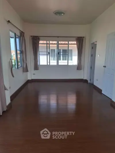 Spacious empty room with wooden flooring and large windows in a modern home.