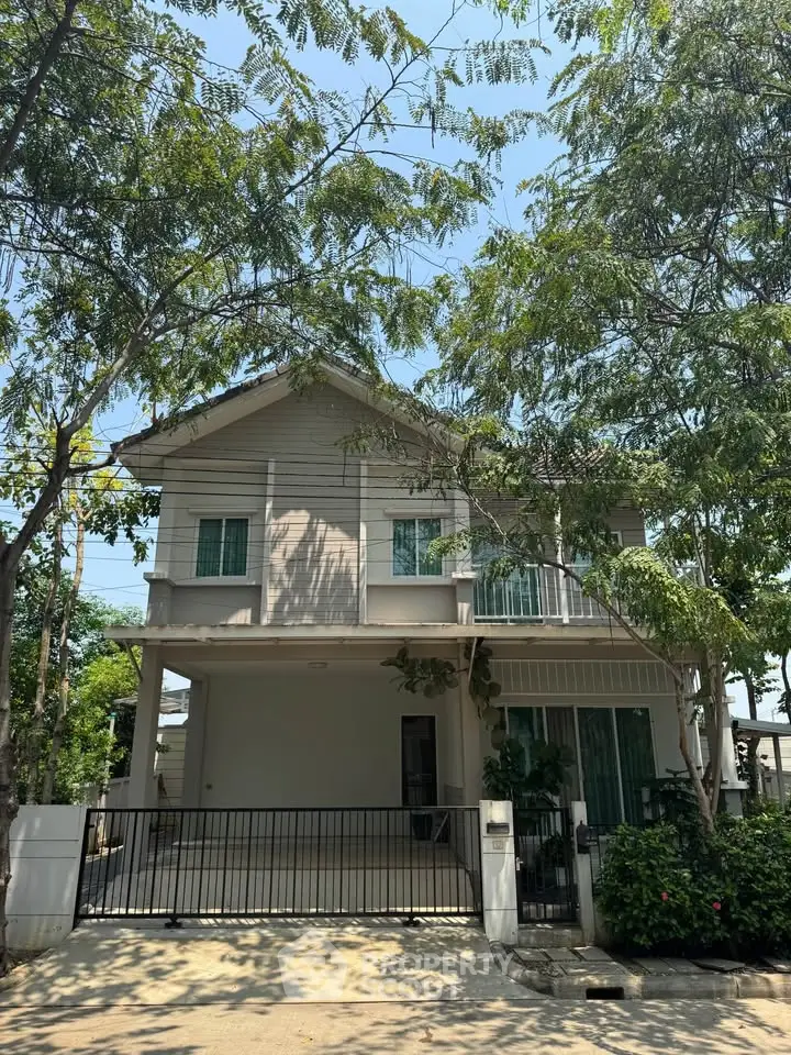 Charming two-story house with lush greenery and gated driveway, perfect for family living.