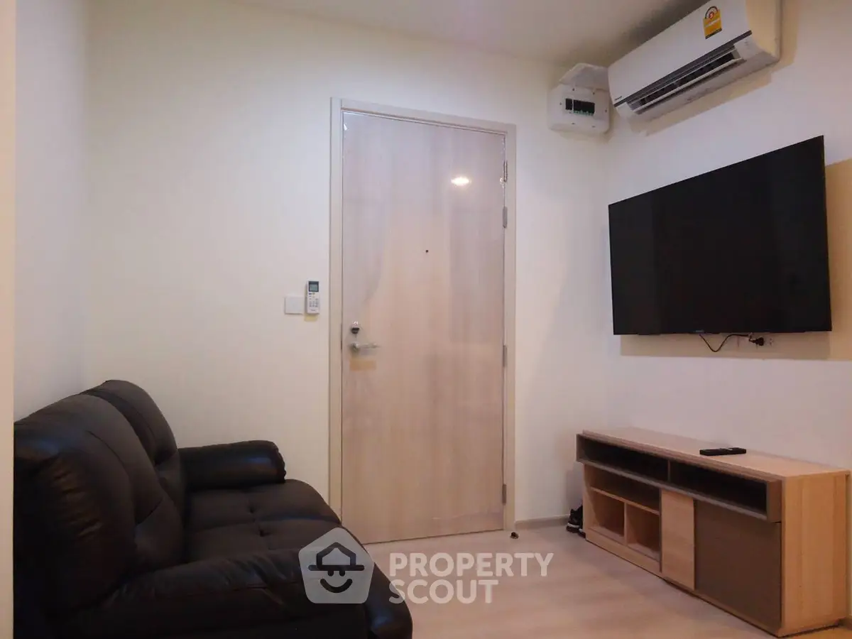 Cozy living room with modern sofa, wall-mounted TV, and air conditioning unit.