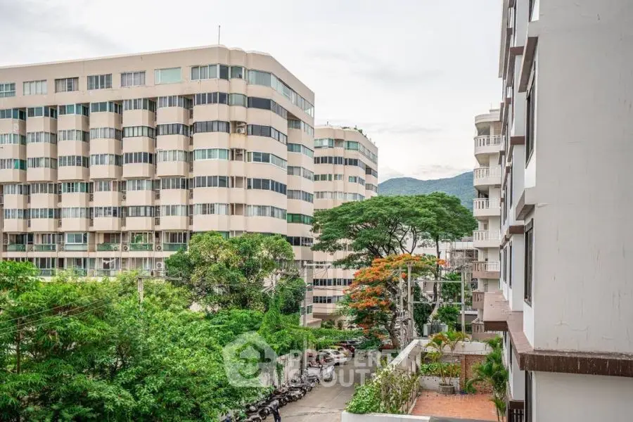 Scenic view of modern apartment buildings with lush greenery and mountain backdrop.