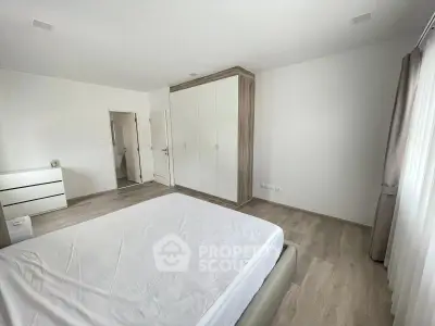 Spacious bedroom with modern design and ample natural light, featuring a large wardrobe and minimalist decor.