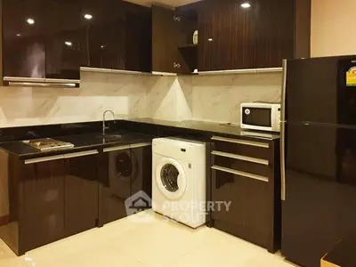 Modern kitchen with sleek dark cabinets, washing machine, and large fridge in stylish apartment.