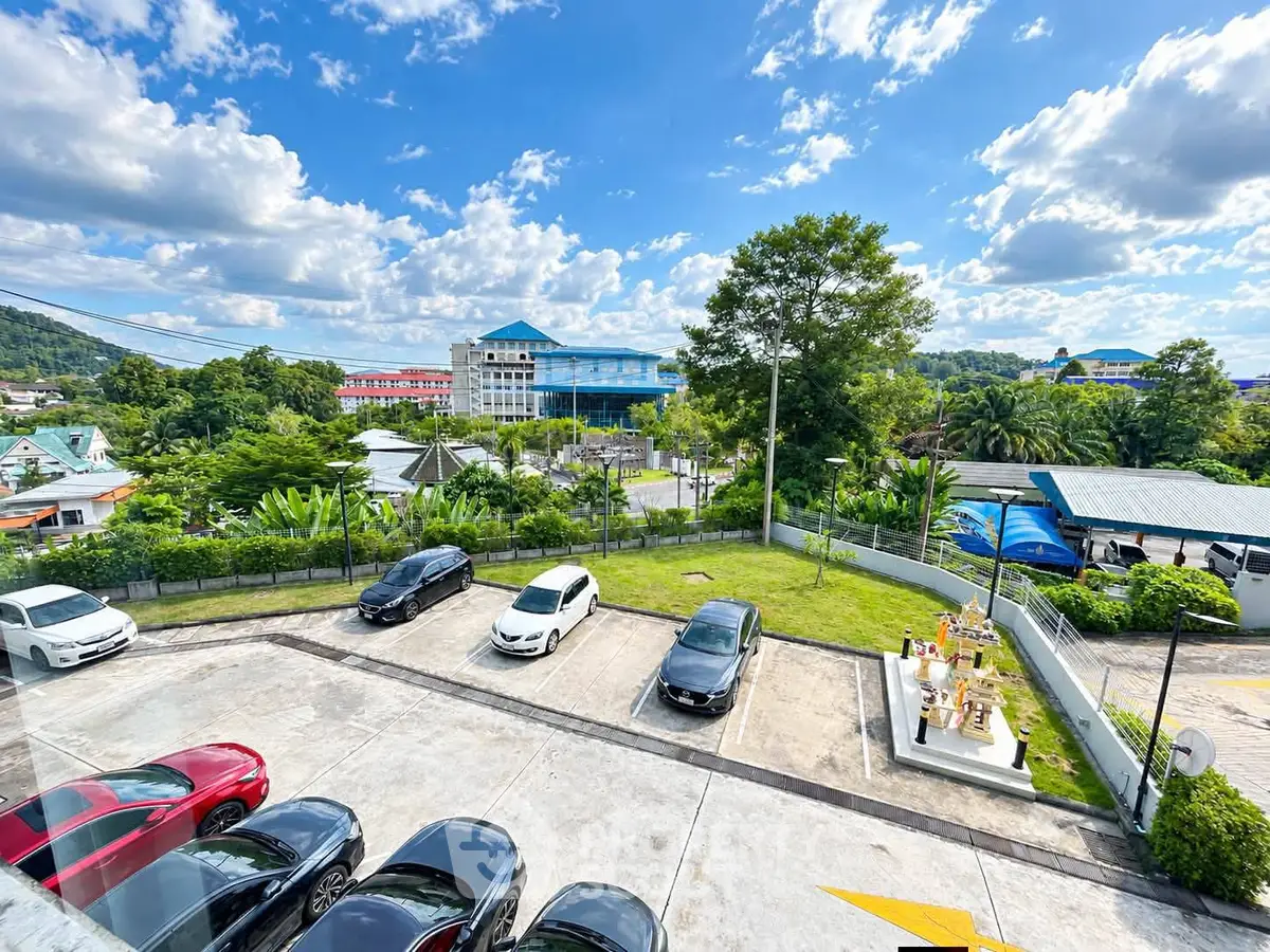 Scenic view from a property overlooking parking area and lush greenery under a vibrant blue sky.