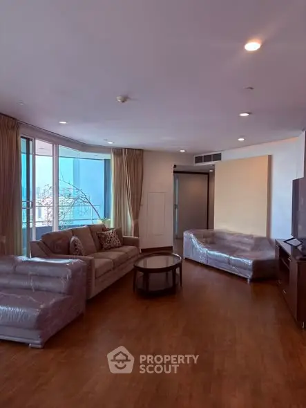 Spacious living room with large windows and modern furniture in a high-rise apartment.