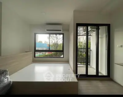 Modern minimalist bedroom with large window and balcony access, featuring sleek design and natural light.