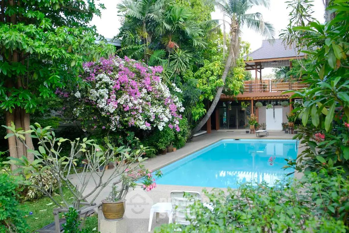 Tropical oasis with lush garden and inviting swimming pool in serene residential setting.