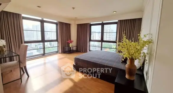 Spacious bedroom with large windows and city view, featuring elegant decor and natural light.