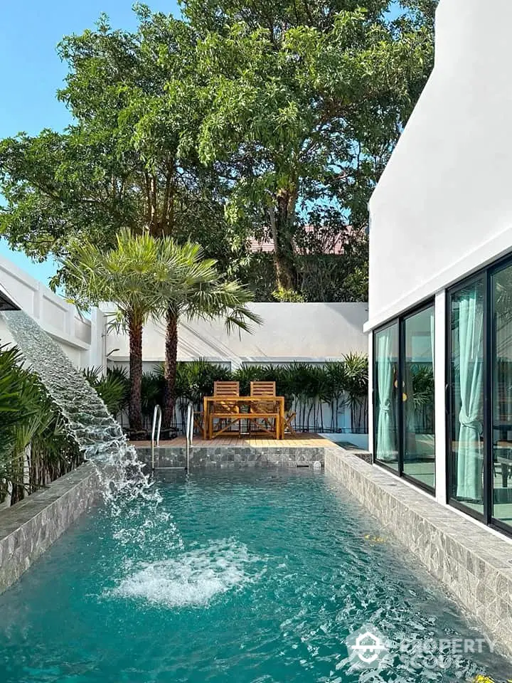 Luxurious private pool with waterfall feature in modern villa surrounded by lush greenery.