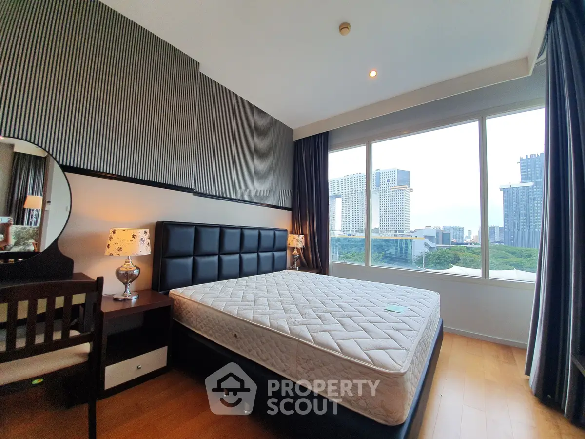 Spacious bedroom with large window offering stunning city view in modern apartment.
