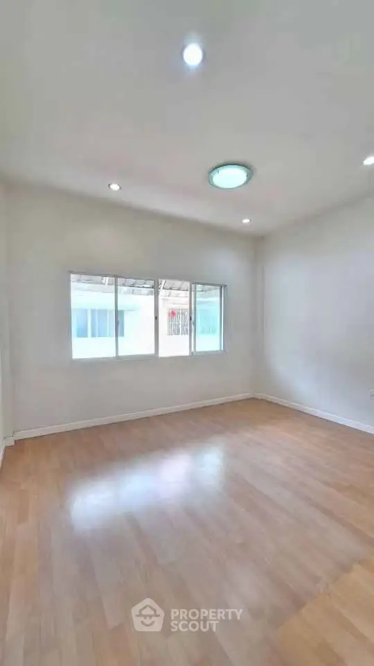 Spacious empty room with wooden flooring and large windows for natural light.