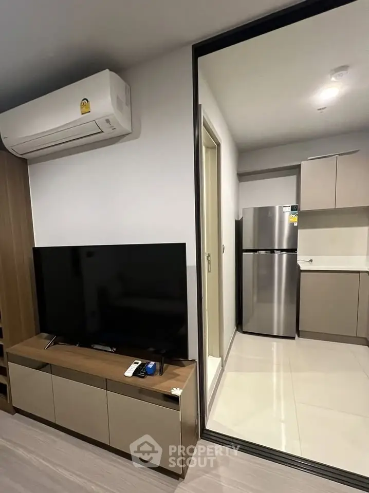 Modern living room with sleek TV unit and view into contemporary kitchen with stainless steel fridge.