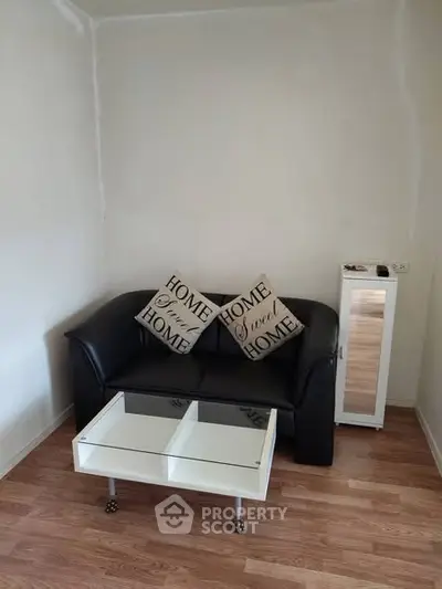 Cozy living room with black sofa, home-themed pillows, and modern coffee table on wooden floor.