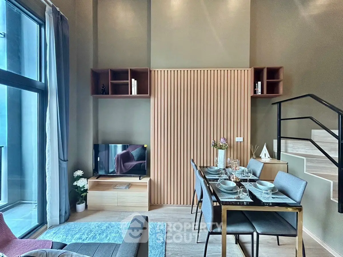 Modern living room with stylish dining area and staircase, featuring large windows and elegant decor.