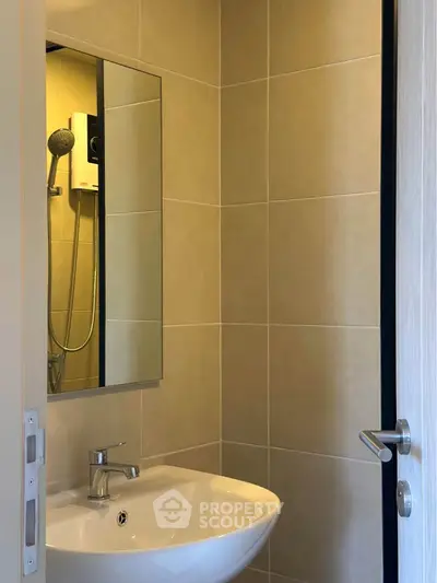Modern bathroom with sleek sink and mirror, featuring a shower in a compact space.