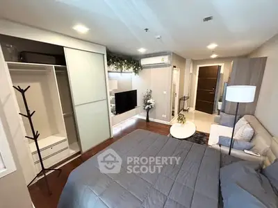 Modern bedroom with open closet, cozy seating area, and wall-mounted TV in stylish apartment.