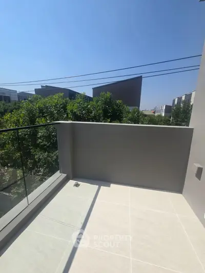 Modern balcony with glass railing and scenic view of greenery and buildings
