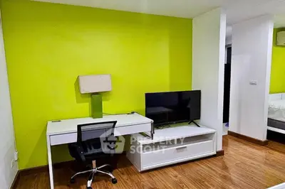 Modern study area with vibrant green wall, sleek desk, and TV setup in stylish apartment.