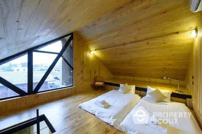 Charming attic bedroom with large geometric window offering ample natural light, nestled in a cozy wooden interior with modern lighting.