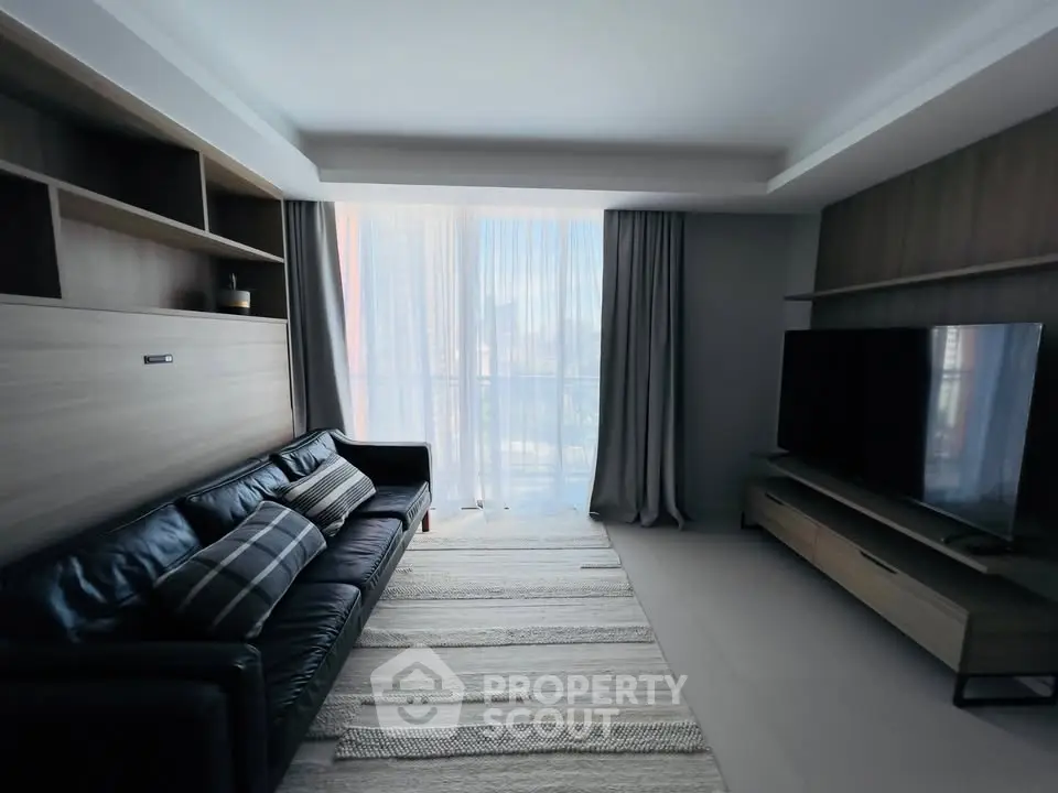 Modern living room with sleek furniture and large TV, featuring floor-to-ceiling windows and stylish decor.