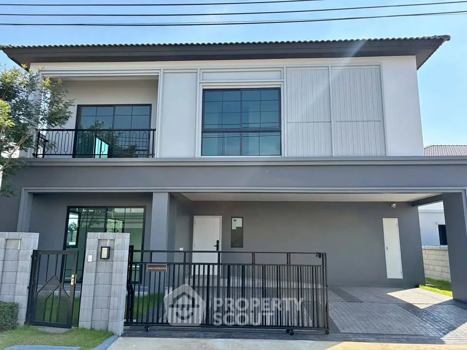 Modern two-story house with sleek design and gated entrance, featuring large windows and a spacious driveway.