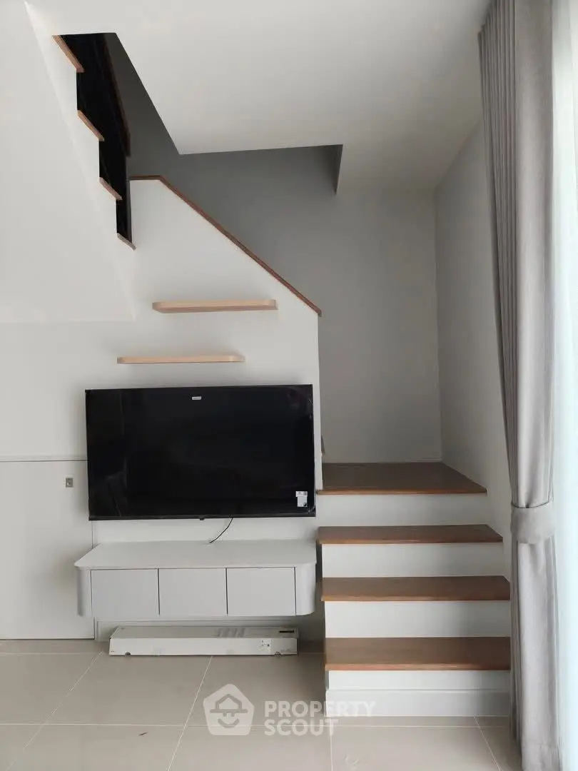 Modern living room with sleek staircase and mounted TV, featuring minimalist design and natural light.