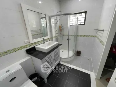 Modern bathroom with sleek black floor tiles, white cabinetry, and a curved glass shower enclosure complemented by green mosaic accents.
