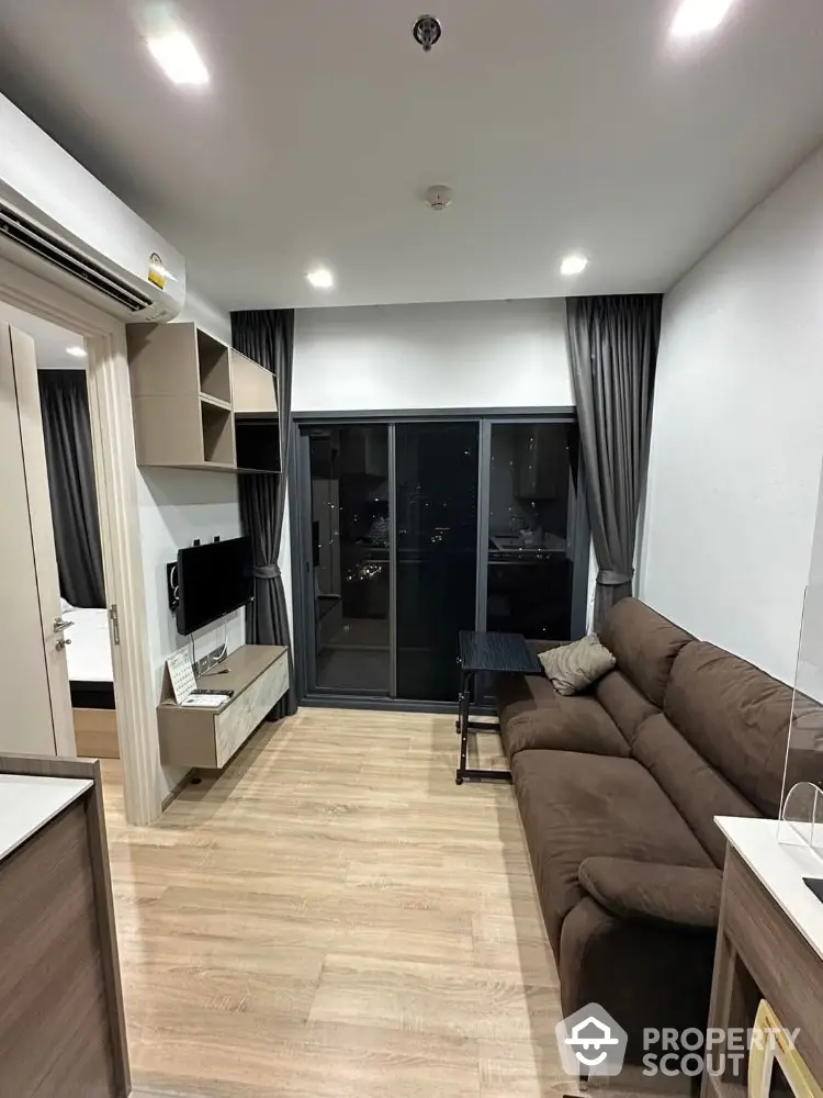 Modern living room with brown sofa and large sliding glass doors leading to balcony.