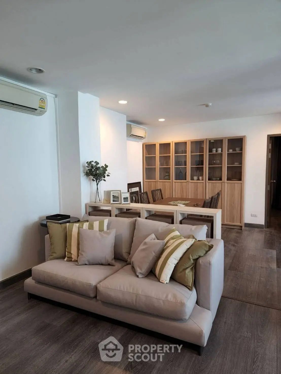 Spacious living room with modern decor and dining area, featuring elegant wooden flooring and stylish furniture.
