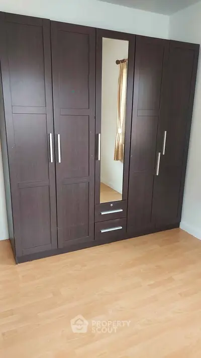 Spacious bedroom with elegant dark wood wardrobe and light wood flooring