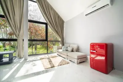 Spacious living room with large windows and modern red fridge, offering serene garden views.
