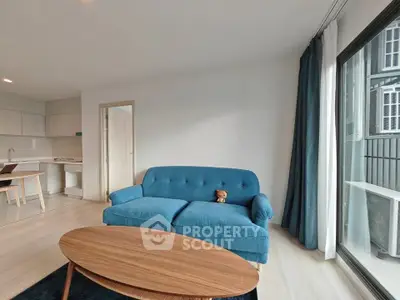 Modern living room with blue sofa and wooden coffee table, featuring large windows and open kitchen layout.