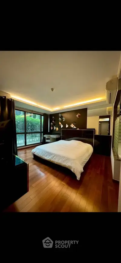 Luxurious bedroom with modern decor and large windows overlooking a lush garden, featuring elegant wooden flooring.