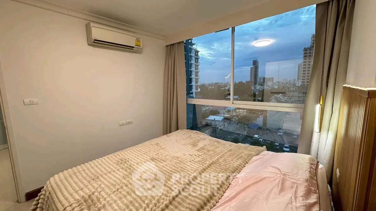 Cozy bedroom with large window offering stunning city view, featuring modern decor and air conditioning.
