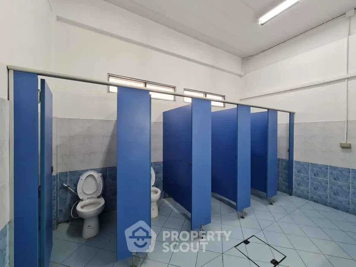 Spacious public restroom with blue stalls and tiled flooring.