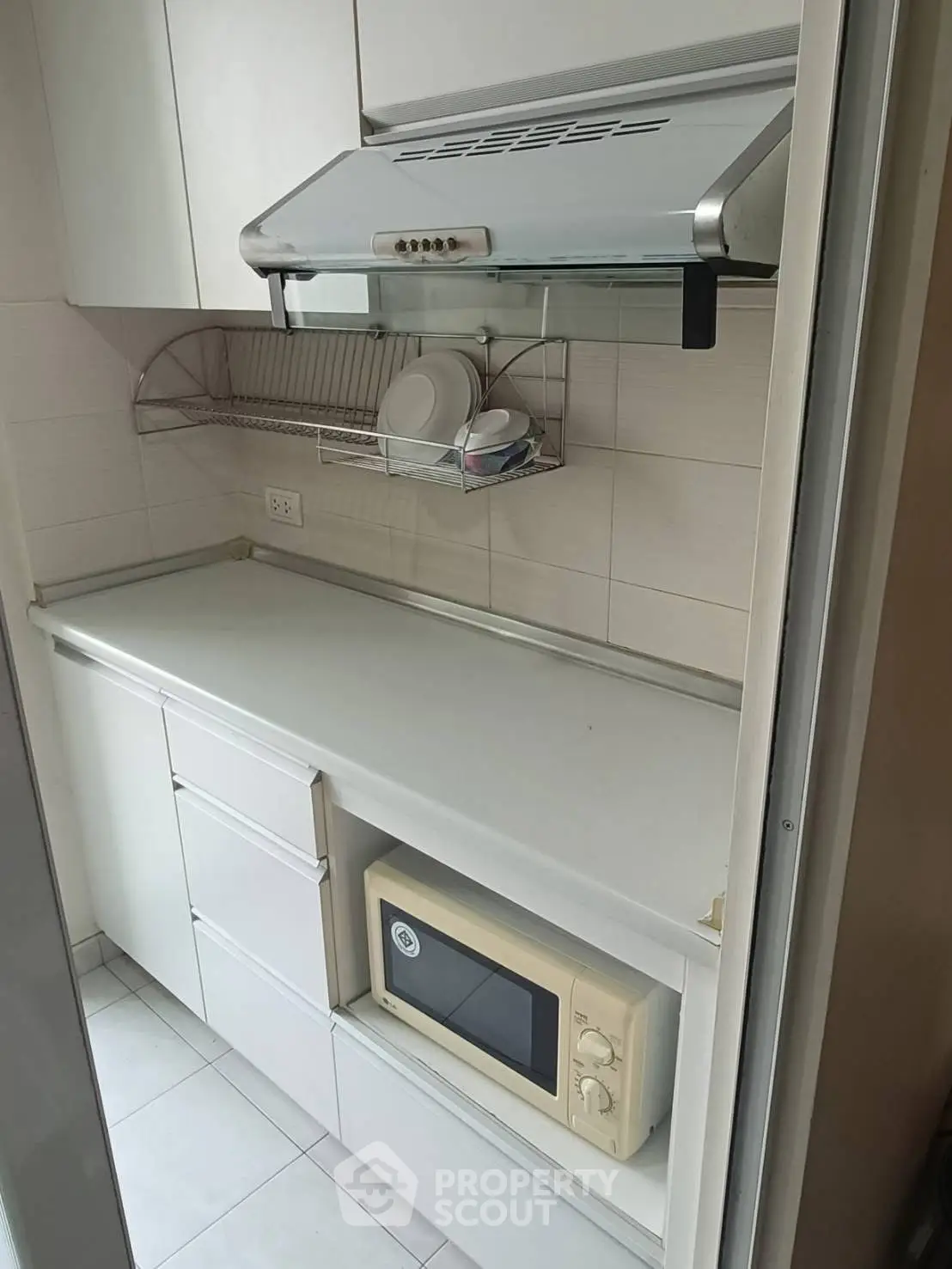 Compact kitchen with microwave and overhead range hood in modern apartment.