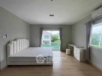Spacious bedroom with large windows and modern furnishings in a serene residential setting.