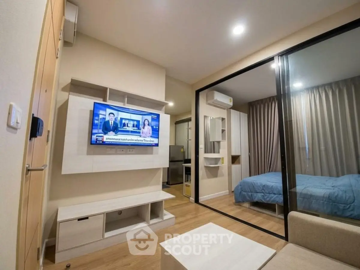 Modern apartment interior with living room and bedroom separated by glass wall, featuring sleek furniture and TV.