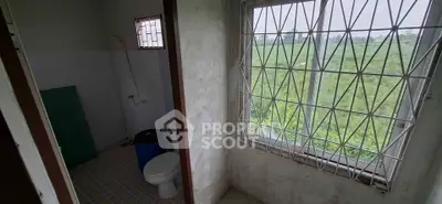 Cozy bathroom with window view of lush greenery, featuring a toilet and tiled floor.