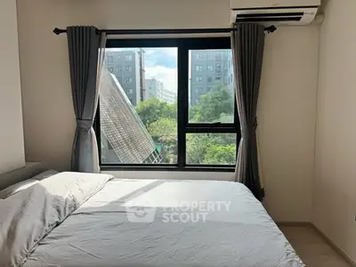 Bright bedroom with large window offering a scenic view of modern buildings and greenery.
