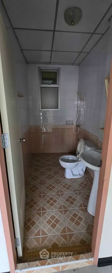 Compact bathroom with tiled floor and wall, featuring a toilet and sink, ideal for small spaces.