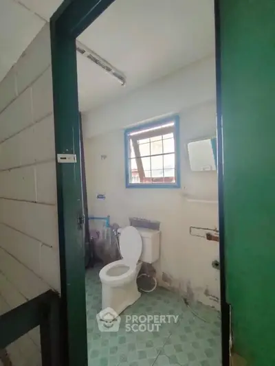 Basic bathroom with green door and window, featuring a toilet and tiled floor.