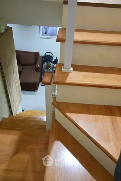 Modern wooden staircase leading to a cozy living area with a brown sofa and exercise equipment.