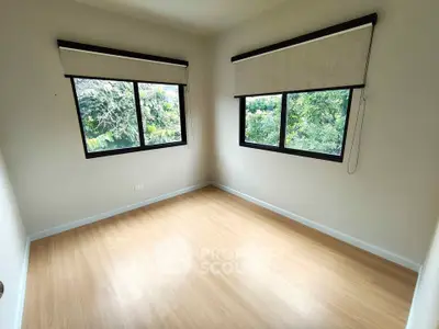 Bright empty room with large windows and wooden flooring, offering lush green views.