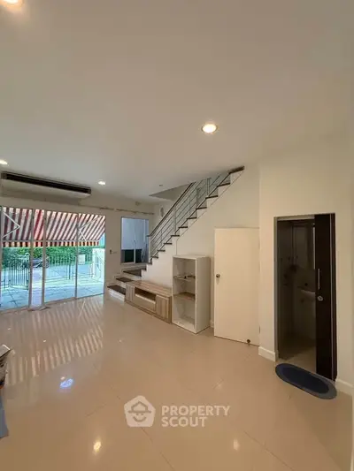 Spacious modern living room with staircase and large windows leading to a patio.