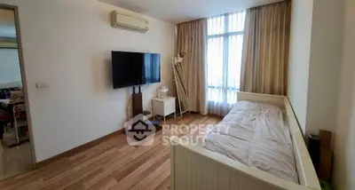 Cozy bedroom with wooden flooring, wall-mounted TV, and large window with curtains.