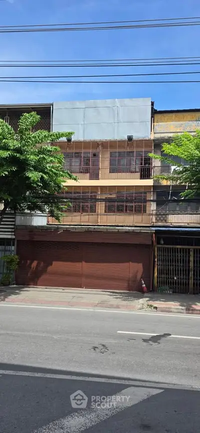 Street view of a commercial building with closed shutters and trees lining the sidewalk.