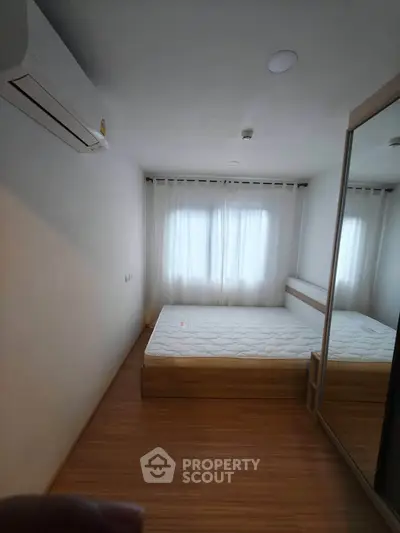 Cozy bedroom with wooden flooring and mirrored wardrobe, featuring a comfortable bed and air conditioning.