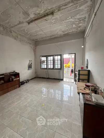Spacious room with tiled floor and large windows, potential for renovation.